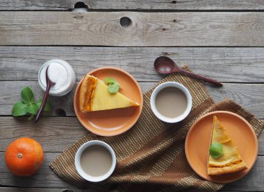 Kremalı ve şekerli çırpılmış yumurtayla kaplı ev yapımı balkabağı turtası ve ahşap bir arka planda bir fincan kahve. Kapat..