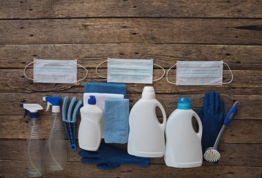 Koronavirüs. Karantina sırasında evi temizleme fikri. Tıbbi koruyucu maskeler ve doğal ahşap arka planda temizlik ve dezenfektanlı plastik molozlar. Evi kullanarak evde vakit geçir..