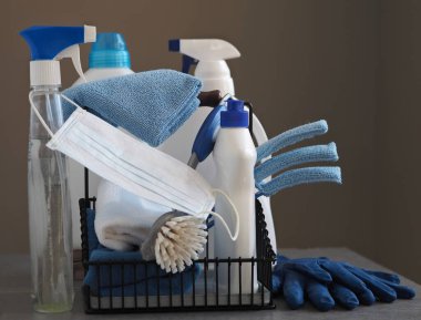 Koronavirüs. Karantina sırasında evi temizleme fikri. Doğal ahşap arka planda çevre temizleyicileri olan plastik tozluklar üzerine tıbbi koruyucu bir maske. Evin kullanımıyla evde vakit geçir..