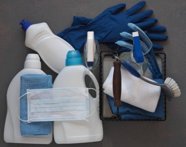 Koronavirüs. Karantina sırasında evi temizleme fikri. Doğal ahşap arka planda çevre temizleyicileri olan plastik tozluklar üzerine tıbbi koruyucu bir maske. Evin kullanımıyla evde vakit geçir..