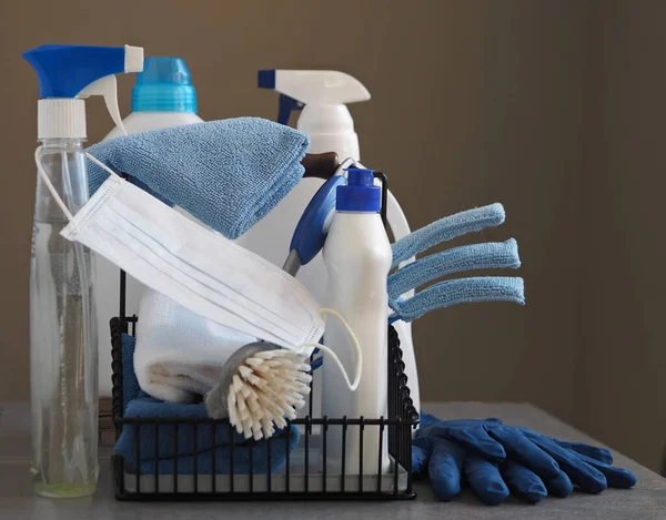 Koronavirüs. Karantina sırasında evi temizleme fikri. Doğal ahşap arka planda çevre temizleyicileri olan plastik tozluklar üzerine tıbbi koruyucu bir maske. Evin kullanımıyla evde vakit geçir..
