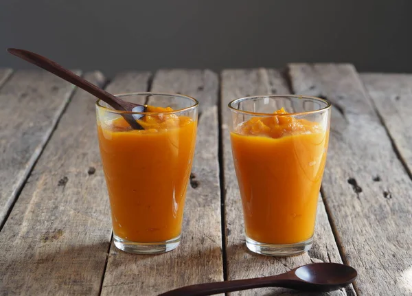 Health benefits of pumpkin. Pumpkin pulp passed through a blender. Eco-friendly smoothie cooked at home on a wooden table and gray background. Home cooking.