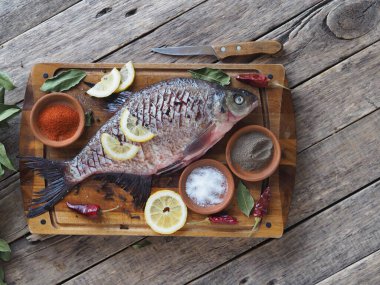 Çiğ nehir çipurası balığı, fırında limon dilimleri ve ahşap bir tahtanın üzerinde baharatla pişirmeye hazır. Üst görünüm, metin için yer.