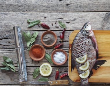 Çiğ nehir çipurası balığı, fırında limon dilimleri ve ahşap bir tahtanın üzerinde baharatla pişirmeye hazır. Üst görünüm, metin için yer.