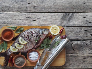 Çiğ nehir çipurası balığı, fırında limon dilimleri ve ahşap bir tahtanın üzerinde baharatla pişirmeye hazır. Üst görünüm, metin için yer.