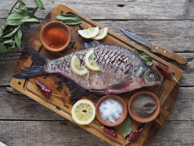 Çiğ nehir çipurası balığı, fırında limon dilimleri ve ahşap bir tahtanın üzerinde baharatla pişirmeye hazır. Üst görünüm, metin için yer.