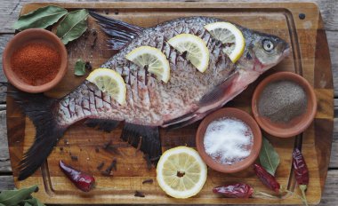 Yakın plan. Çiğ nehir balığı, fırında pişirmek için limon dilimleri ve ahşap bir tahtanın üzerinde baharat ile pişirilir. Yan görünüm.