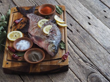 Yakın plan. Çiğ nehir balığı, fırında pişirmek için limon dilimleri ve ahşap bir tahtanın üzerinde baharat ile pişirilir. Ön görünüm.