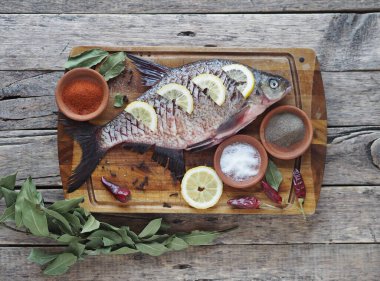 Yakın plan. Çiğ nehir balığı, fırında pişirmek için limon dilimleri ve ahşap bir tahtanın üzerinde baharat ile pişirilir. Yan görünüm, metin için yer