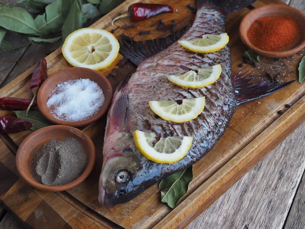Yakın plan. Çiğ nehir balığı, fırında pişirmek için limon dilimleri ve ahşap bir tahtanın üzerinde baharat ile pişirilir. Ön görünüm.