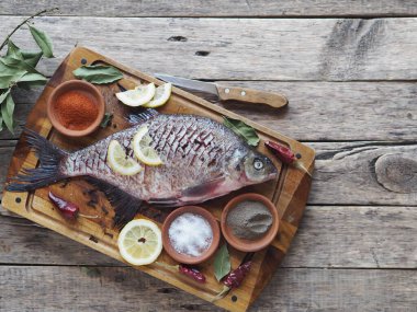 Çiğ nehir çipurası balığı, fırında limon dilimleri ve ahşap bir tahtanın üzerinde baharatla pişirmeye hazır. Üst görünüm, metin için yer.