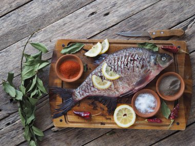Çiğ nehir çipurası balığı, fırında limon dilimleri ve ahşap bir tahtanın üzerinde baharatla pişirmeye hazır. Üst görünüm, metin için yer.