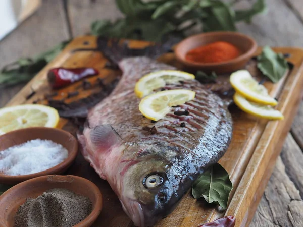 Close-up. Raw river fish of bream cooked for baking in the oven with slices of lemon and seasoning on a wooden board. Front view.