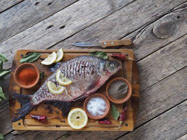 Çiğ nehir çipurası balığı, fırında limon dilimleri ve ahşap bir tahtanın üzerinde baharatla pişirmeye hazır. Üst görünüm, metin için yer.