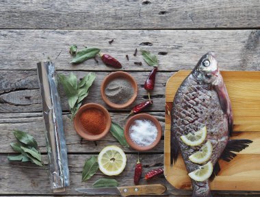 Çiğ nehir çipurası balığı, fırında limon dilimleri ve ahşap bir tahtanın üzerinde baharatla pişirmeye hazır. Üst görünüm, metin için yer.
