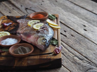 Yakın plan. Çiğ nehir balığı, fırında pişirmek için limon dilimleri ve ahşap bir tahtanın üzerinde baharat ile pişirilir. Ön görünüm.