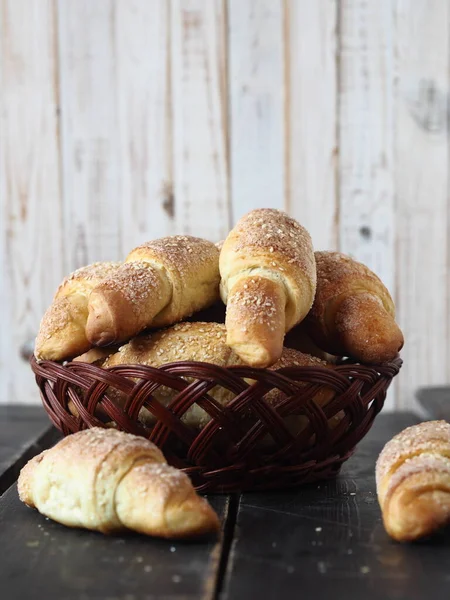 Homemade cakes croissants, sprinkled with sesame and sugar, in a natural plate made of vine on a dark wooden background.