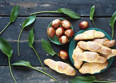 Paskalya. Yumurta boyalı soğan kabuğu ve ev yapımı kruvasan yeşil yapraklı, koyu renk ahşap arka planda doğal bir asma tabakasında pişirilmiş..
