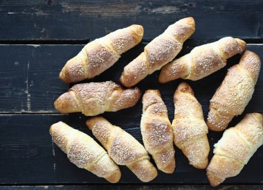 Koyu ahşap zemin üzerine susam ve şeker serpiştirilmiş kruvasanlar. Ev yapımı kek..