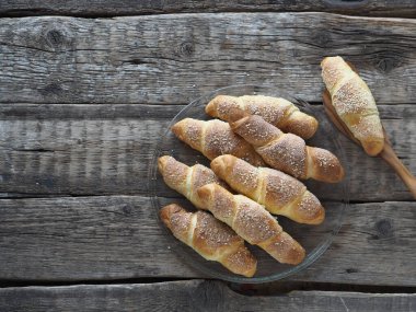 Eski bir ahşap zemine susam ve şeker serpiştirilmiş kruvasanlar. Ev yapımı kek..