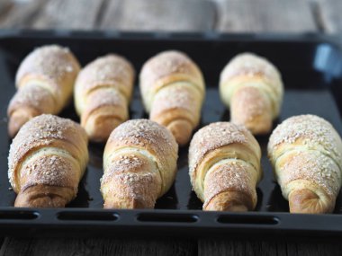 Eski ahşap bir arka planda, fırının tepsisine susam ve şeker serpiştirilmiş kruvasanlar. Ev yapımı kek..