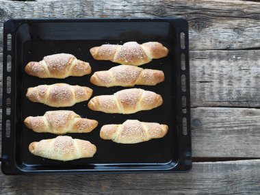 Eski ahşap bir arka planda, fırının tepsisine susam ve şeker serpiştirilmiş kruvasanlar. Ev yapımı kek..