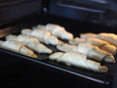 Mutfak fırınının tepsisine susam ve şeker serpiştirilmiş kruvasanlar pişirilmeye hazır. Ev yapımı kek..