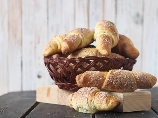 Croissants, sprinkled with sesame and sugar, in a natural vine plate on a dark wooden background.Homemade cake.