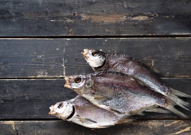 Koyu ahşap bir arka planda, havadan kurutulmuş tuzlu tatlı su çipinin yakın plan çekimi. Üç parça..