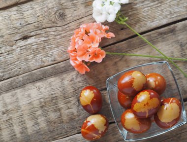 Paskalya geçmişi. Mesaj için yer. Cam bir tabağa boyanmış yumurta, ahşap bir arka planda çiçekler..