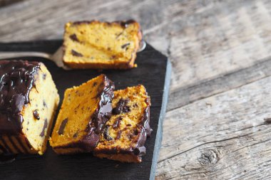 Çikolatalı, yumuşak balkabaklı kek, üzerine dilimlenmiş çikolata serpiştirilmiş, siyah bir mutfak tahtası. Ahşap antik arkaplan.