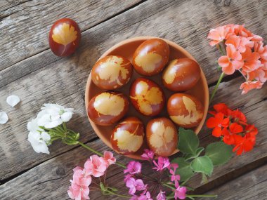 Paskalya geçmişi. Yumurtalar kilden bir tabakta soğan kabuğu ve pelargonyum çiçekleri, doğal ahşap bir arka planda..