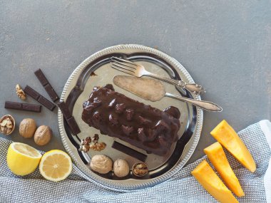 Çikolatalı balkabaklı kek, jöleli çikolata, metal bir tabakta yemek pişirmek için malzemelerle dolu gri bir kırsal masada..