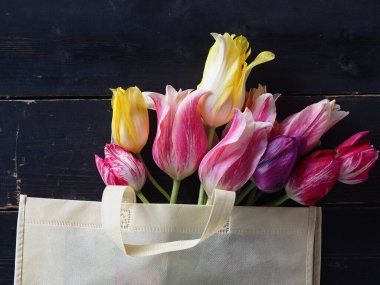 Koyu ahşap bir masada doğal bir kumaş torba içinde taze lale çiçekleri. Boşluğun bir kopyasıyla en üstteki görünüm.
