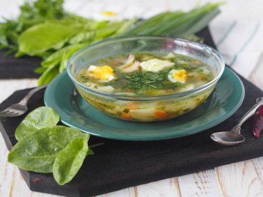 Sağlıklı yiyecek. Bir kase yeşil talaş çorbası beyaz ahşap bir masada yeşil malzeme yığınının arka planına karşı..