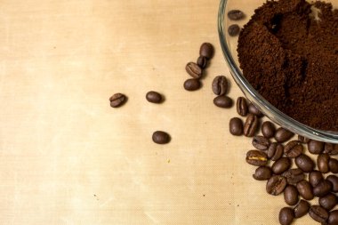 Kahve fonu. Doğal kavrulmuş kahve çekirdekleri ve cam bir kâsede şeffaf kahve masanın üzerinde doğal bej kumaş arka plan, Kopi uzayından yan görüş.