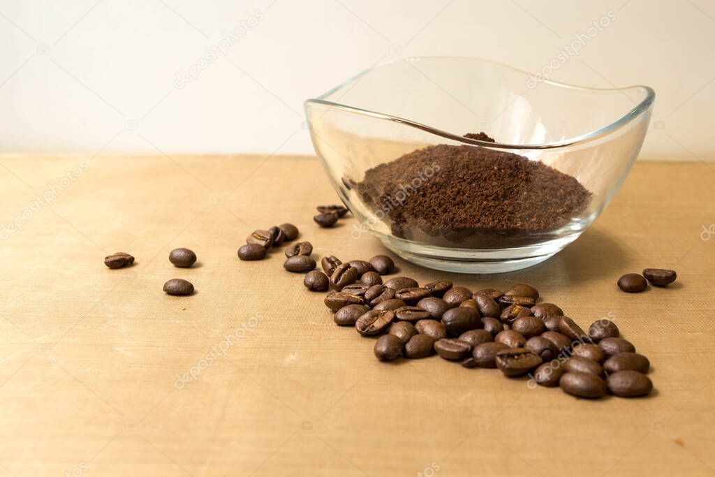 Coffee background. Natural roasted coffee beans and ground coffee in a glass transparent bowl on a natural beige fabric background on the table, side view from Kopi space