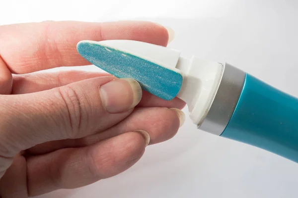 Manicure at home. An electric nail file with diamond dusting in the unkempt hands of a woman doing a close-up manicure