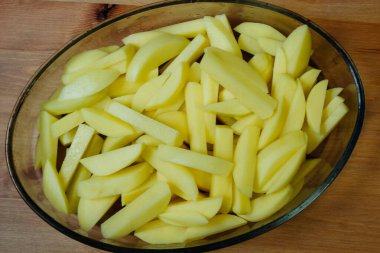 Kızartmadan patates pişirmek. Çiğ patates, şerit şeklinde kesilmiş ve cam oval ısıya dayanıklı tabakta pişirmek için pişirilmiş ahşap bir masada yakın plan.