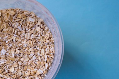 Sağlıklı besinler: Glüten içeren tahıllar. Yulaf ezmesi (Herkül), büyük ürünleri Kopi alanı olan mavi bir arkaplanda saklamak için yuvarlak plastik bir kapta saklanır..