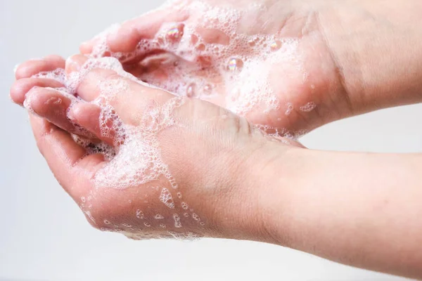 Hygiene and protection of hands from viruses (coronavirus) and bacteria using soap. Women\'s hands with foamed soap close-up on a white background. The process of properly washing hands with soap.