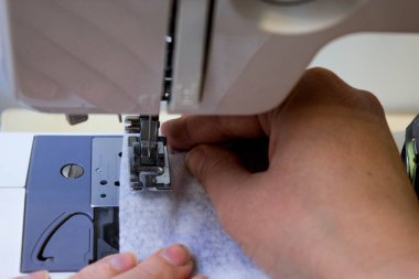Evde dikiş makinesine dikiş dikiyorum. Korunmaya ve koronavirüsten korunmaya ihtiyacı olanlar için tıbbi maske üretimi ve dikimi. Terzi elleri yakın.