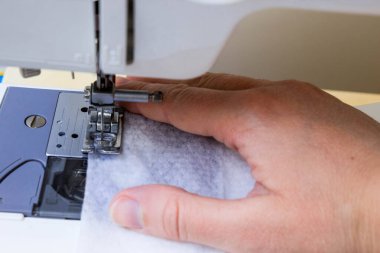 Evde dikiş makinesine dikiş dikiyorum. Korunmaya ve koronavirüsten korunmaya ihtiyacı olanlar için tıbbi maske üretimi ve dikimi. Terzi elleri yakın.