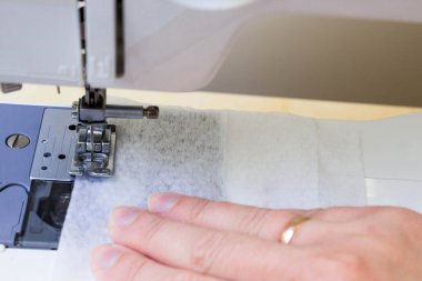Evde dikiş makinesine dikiş dikiyorum. Koronavirüsten korunması ve korunması gereken kişiler için maske üretimi ve dikiş ekipmanları Maske sıkıntısı çekenlere karşı