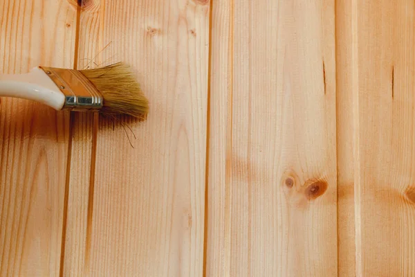 Paint coating and protection of wooden surfaces. A brush covering a pine wood wall with center-beaded board varnish for interior work, with copy space.