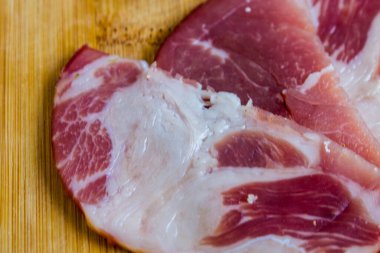 Çiğ domuz eti servis ediyorum. Çiğ tütsülenmiş domuz boynu ve ahşap bir bambu tahtasına yakın plan detaylı bir tabaka..