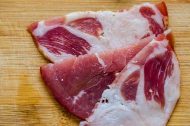 Çiğ domuz eti servis ediyorum. Çiğ tütsülenmiş domuz boynu ve ahşap bir bambu tahtasına yakın plan detaylı bir tabaka..