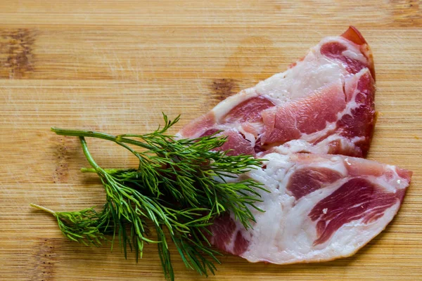Serving raw smoked pork. Slices of raw smoked pork neck detailed in close up with dill twigs on a wooden bamboo Board with Copy space for text