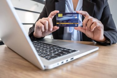 İş kadını dizüstü bilgisayar kullanıyor ve ödeme için kredi kartı tutuyor