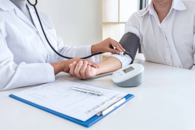Doctor using stethoscope checking measuring arterial blood pressure on arm to a patient in the hospital, healthcare and medical concept.